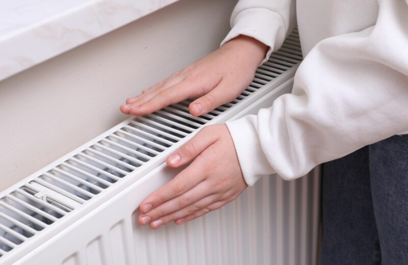 Ihminen kokeilemassa lämpöpatterin lämpötilaa käsillään.